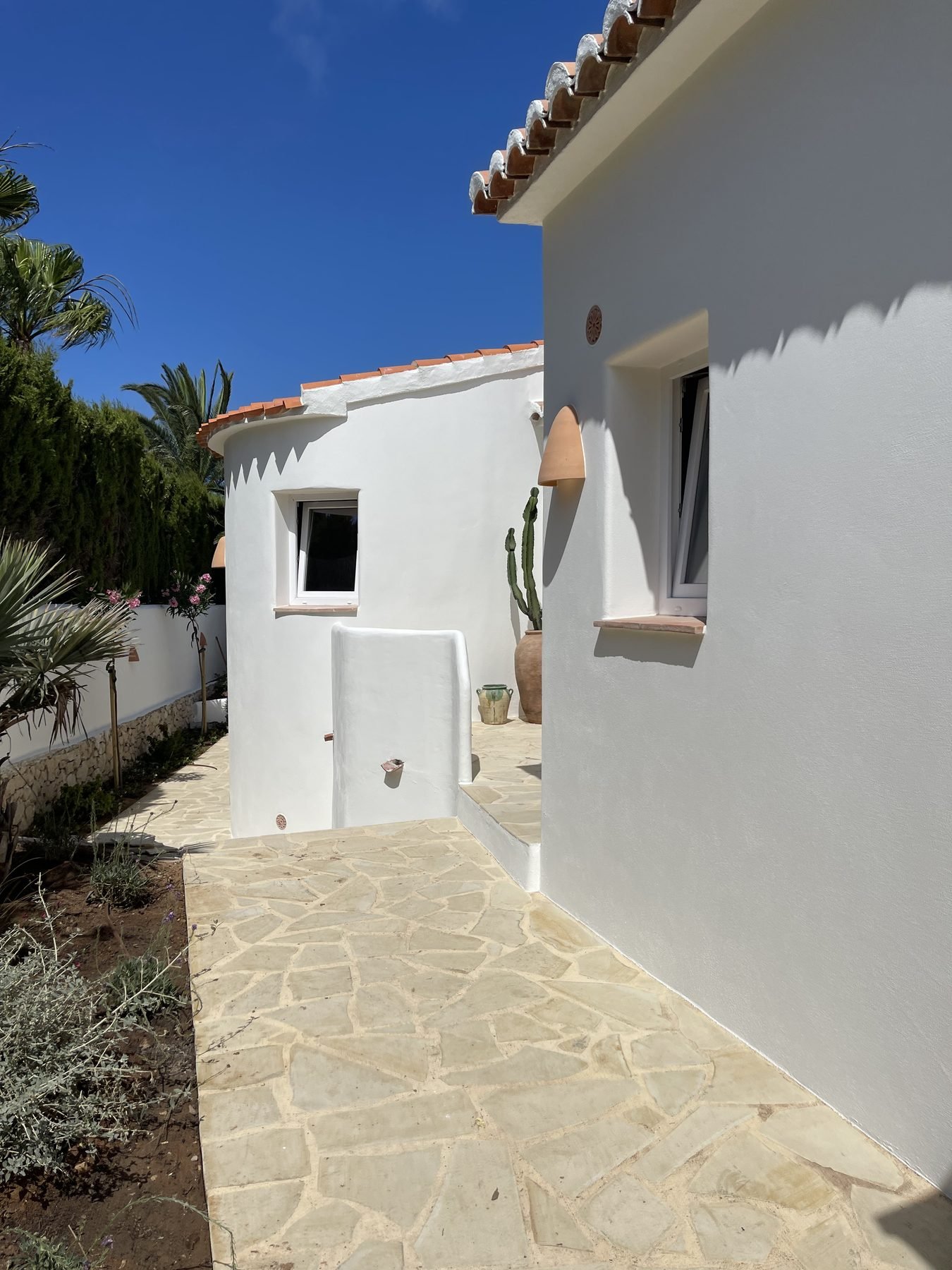 Fachada blanca recién pintada de Villa Mozart con patio de piedra natural en Jávea