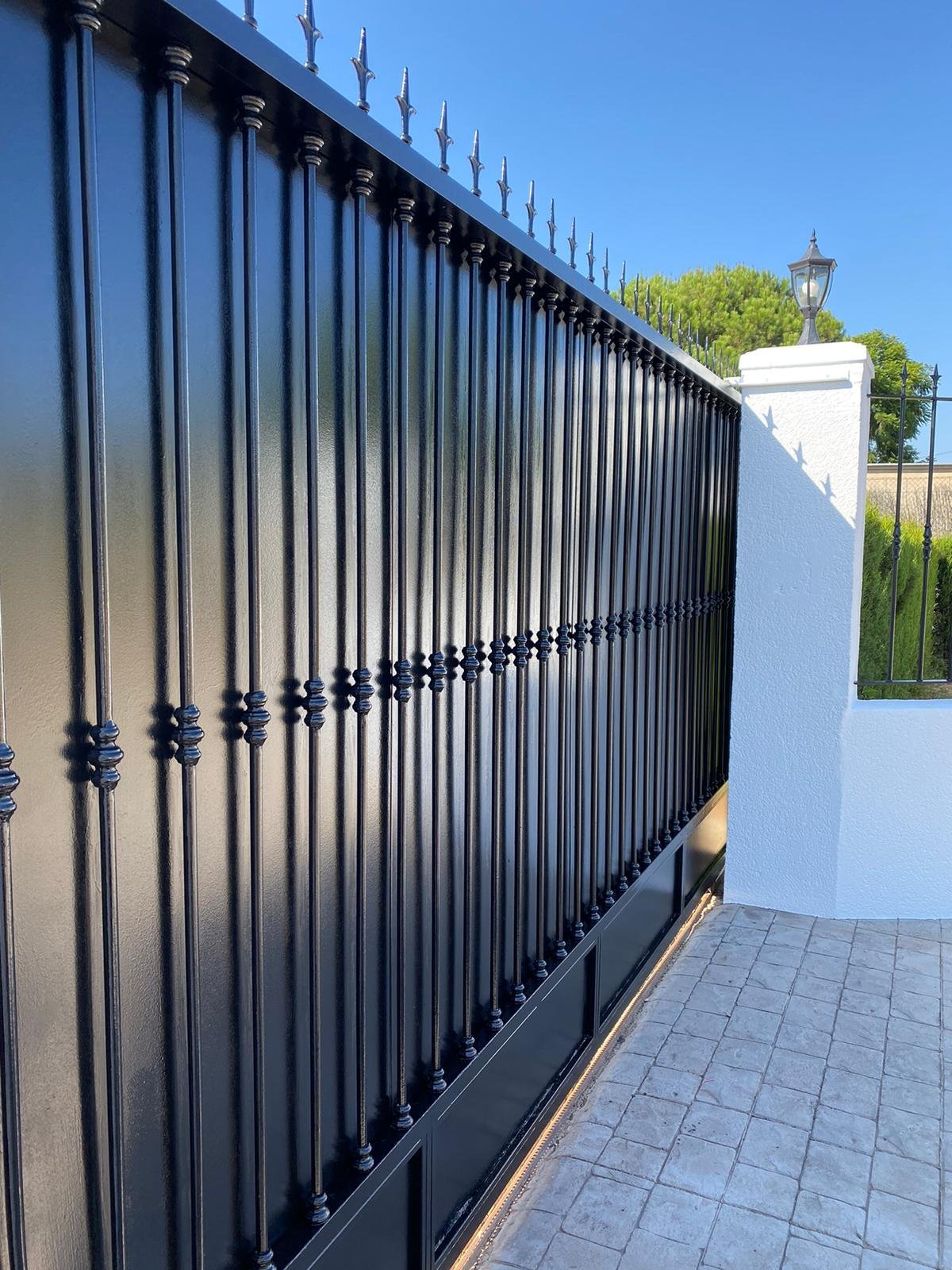 Verja de forja negra recién pintada junto a muro blanco