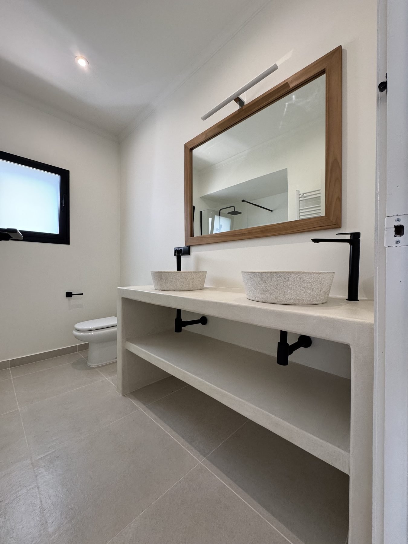 Baño en microcemento con doble lavabo de piedra y mueble en Casa Gafarro, Jávea